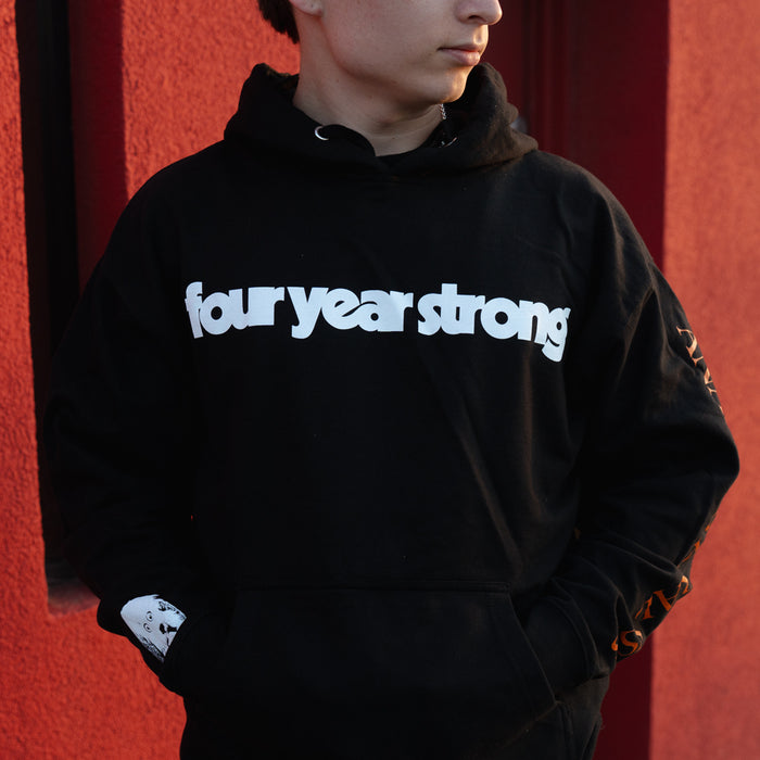 Wearing a Four Year Strong printed hoodie with the band name in bold white letters, a person stands against a red wall, looking to the side with hands in the front pocket.