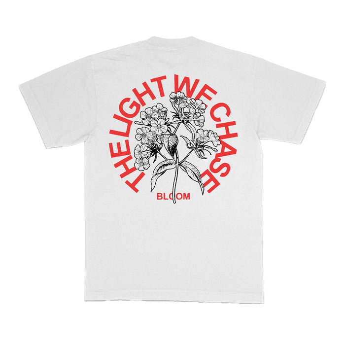 The Bloom white T-shirt showcases a bold black floral illustration on the back, with red arched text reading THE LIGHT WE CHASE and BLOOM printed in red below the design.