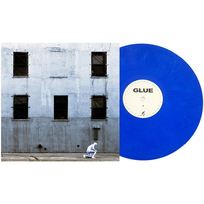 A Boston Manor Electric Blue Galaxy vinyl labeled GLUE sits next to its album cover, showing a person in a white suit crouching before a weathered gray building with barred windows.