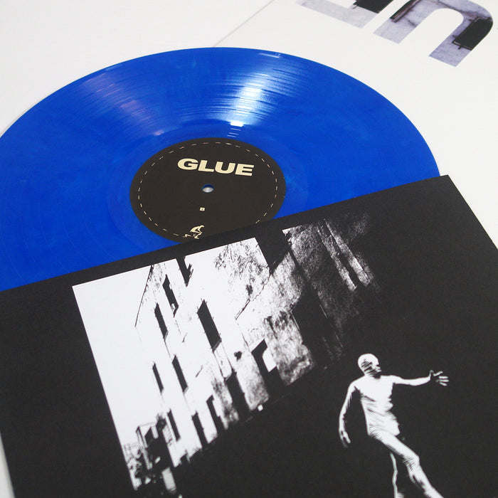 A blue vinyl record labeled GLUE by Boston Manor—resembling the Electric Blue Galaxy—partially slides out from a black-and-white album cover with a high-contrast photo of a building and a person in motion.