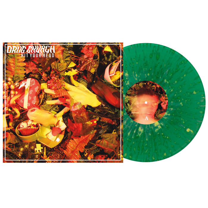 The image shows a neon yellow splatter vinyl record next to its album cover, which features yellow gloves among red and green foliage. This is the Hit Your Head vinyl from the brand Drug Church.