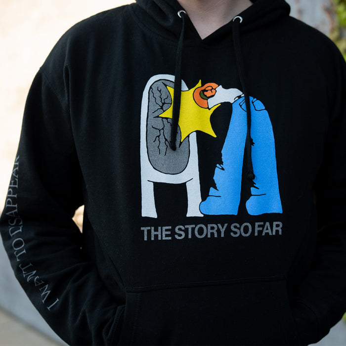 A person wears a black Independent Midweight sweatshirt by The Story So Far, featuring a vibrant graphic of two cartoon figures and the bands name on the front, with partially visible white text on the left sleeve for added flair.
