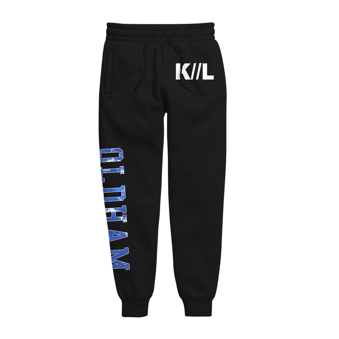 Black cotton joggers by Knocked Loose featuring an elastic waistband, drawstring, white K/L logo on the left thigh, and bold blue and white OLIDTEAM lettering on the right leg—ideal for a stylish look.
