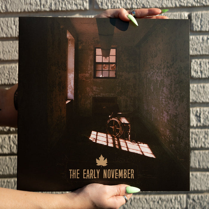 A person with long, green-painted nails holds The Early Novembers Eco Mix Lavender Vinyl, showcasing cover art of a dimly lit, empty room with a wheelchair and light streaming through the window.