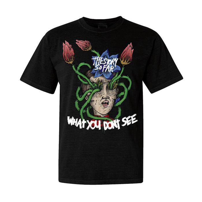 The Story So Far black T-shirt in midweight fabric features a face graphic wrapped in green vines and red flowers. “THE STORY SO FAR” is printed above, with “WHAT YOU DON’T SEE” below in distressed white and red text.