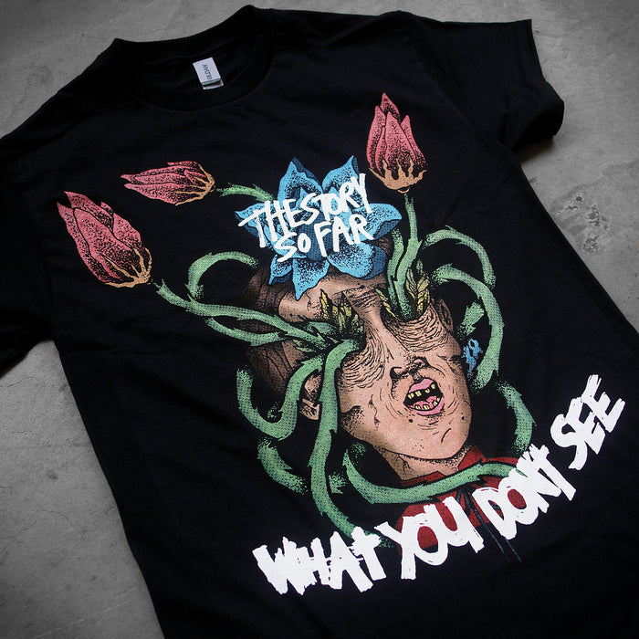 A black 100% cotton tee from The Story So Far featuring a surreal face with tentacles and flowers, their name on the forehead, and What You Dont See in bold at the bottom.
